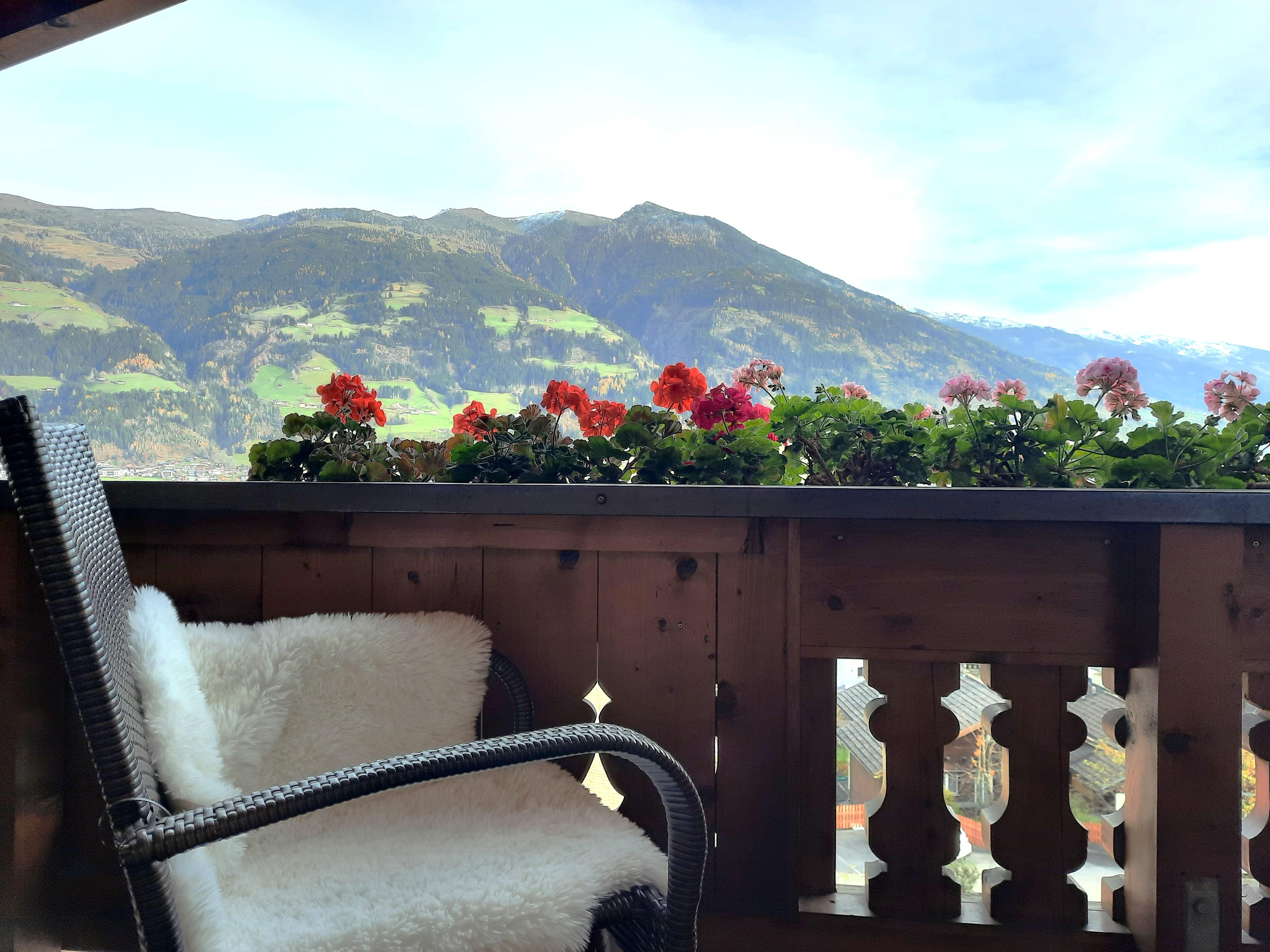 Blick auf einen Balkon mit Blumen und Berglandschaft im Hintergrund, inklusive Wolken und Himmel.