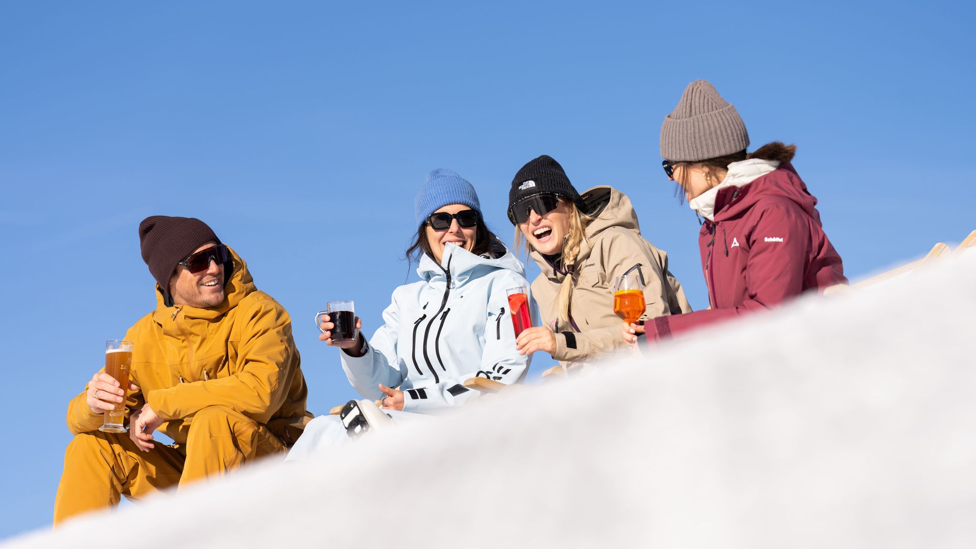Sonniger Frühlingsskilauf in Mayrhofen: Vier Freunde genießen die warme Märzsonne in Liegestühlen auf einer Skihütte im Zillertal. Entspannte Pause bei kühlen Getränken und Alpenpanorama.