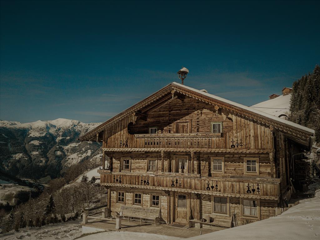 A wooden chalet in snowy mountain scenery under a clear sky.