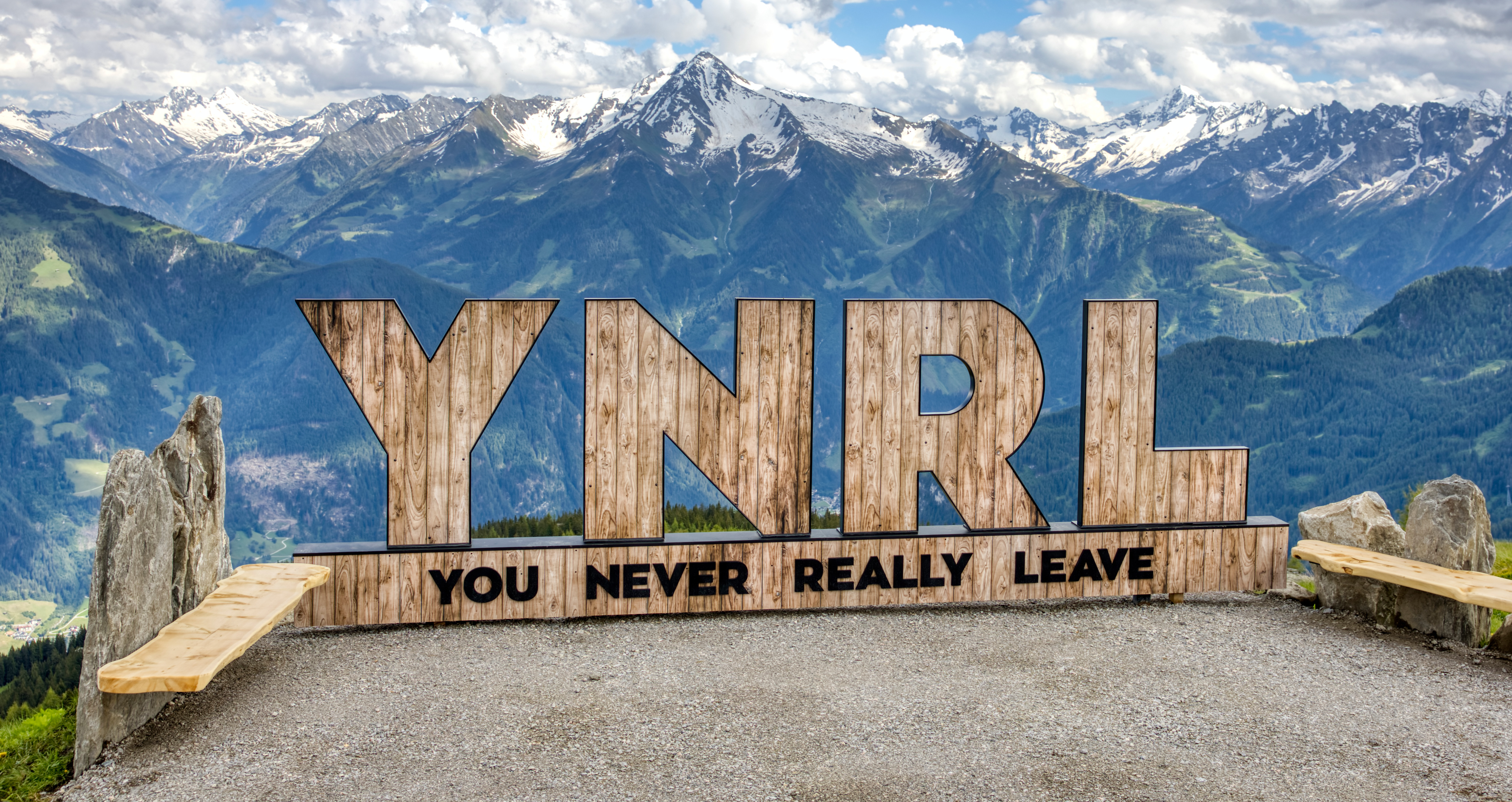 Holzskulptur YNRL vor Zillertaler Alpenpanorama als Einleitung zu den FAQs. Das Bild steht für bleibende Erinnerungen durch bestens informierte Urlaubsplanung in Mayrhofen-Hippach – von der Anreise bis zum Skipass.