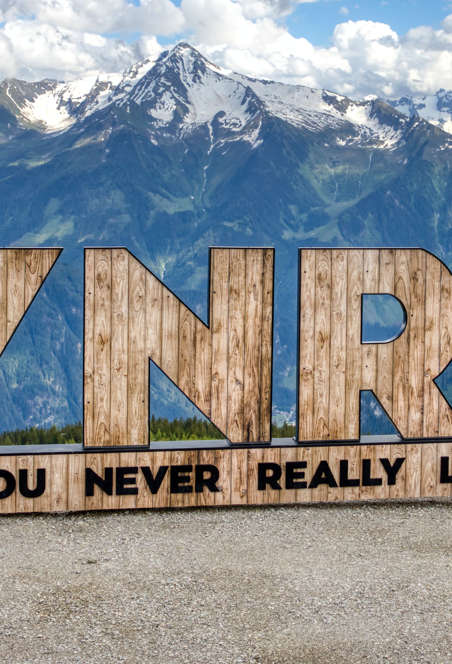 YNRL wooden landmark in front of the Zillertal Alps, introducing the Mayrhofen-Hippach FAQ section. Representing the lasting memories created through well-informed travel planning, from transport to lift passes.