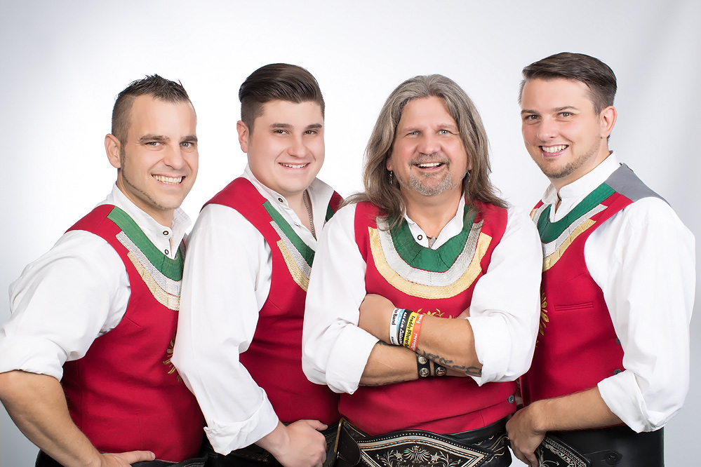 Fünf Männer in traditionellen Trachten, lächelnd, vor hellem Hintergrund, vermutlich die Freddy Pfister Band.
