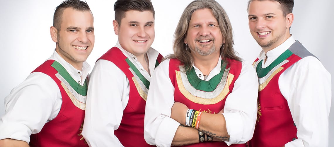 Fünf Männer in traditionellen Trachten, lächelnd, vor hellem Hintergrund, vermutlich die Freddy Pfister Band.