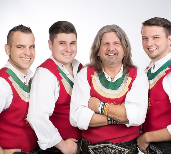 Fünf Männer in traditionellen Trachten, lächelnd, vor hellem Hintergrund, vermutlich die Freddy Pfister Band.