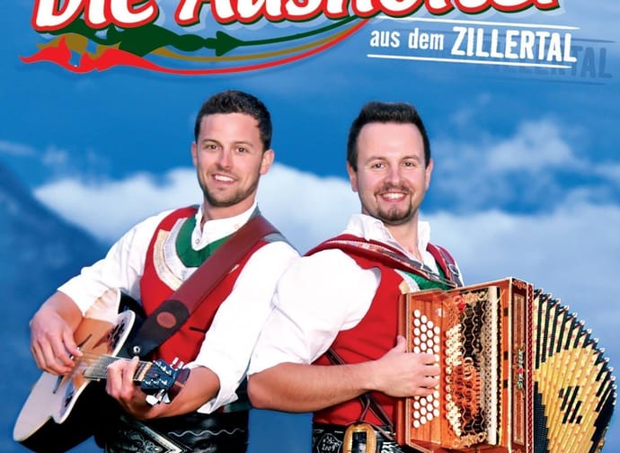 Das Bild zeigt die Gruppe "Die Ausholter" mit einem Musikanten mit Gitarre und einem Musikanten mit einer Ziehharmonika.
