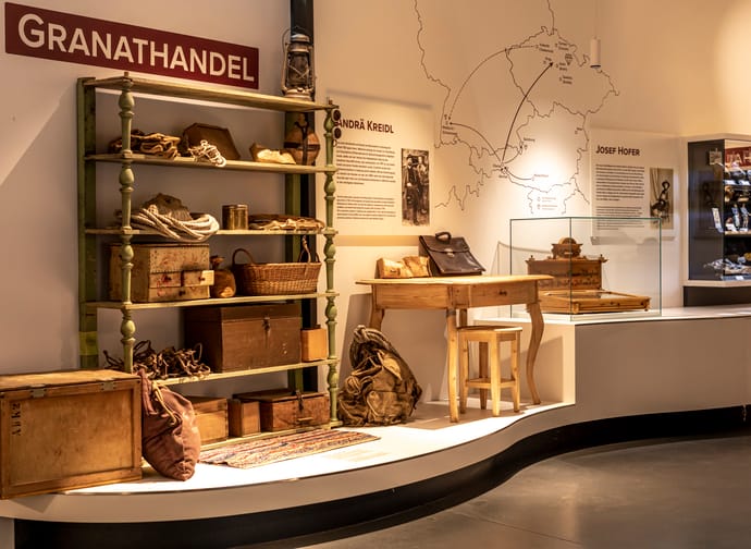 Exhibit with vintage items, boxes, bags, a wooden desk, and informational panels on the wall in a museum.