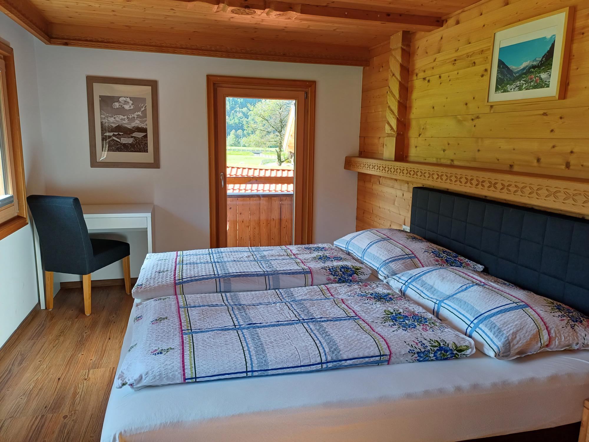Bedroom with two beds, wooden walls, window, and a small desk with chair, view outside.