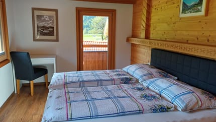 Bedroom with two beds, wooden walls, window, and a small desk with chair, view outside.