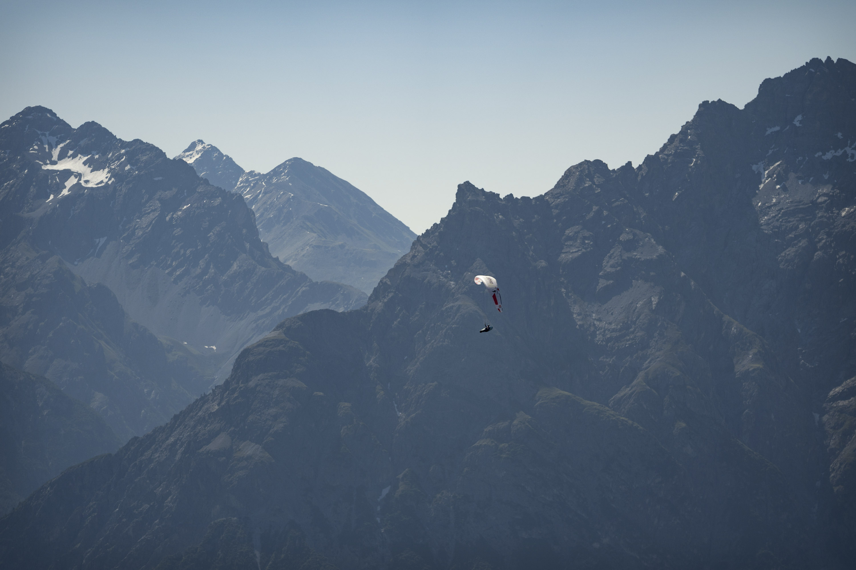 Das Bild zeigt einen Paragleiter beim Fliegen mit einer massiven Bergkulisse im Hintergrund.