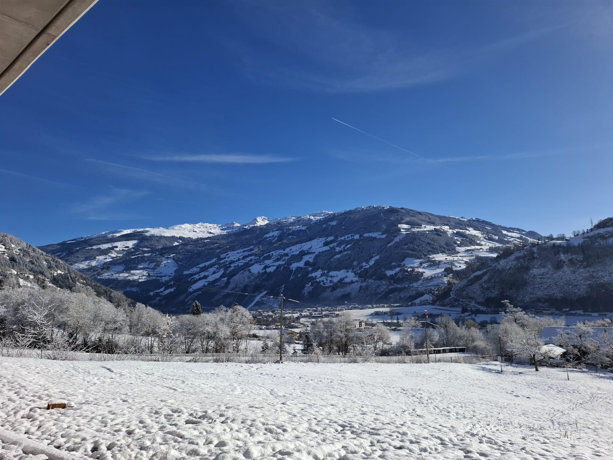 Schneebedeckte Berge unter klarem blauen Himmel, einige Wolken und eine Flugzeugspur sichtbar.