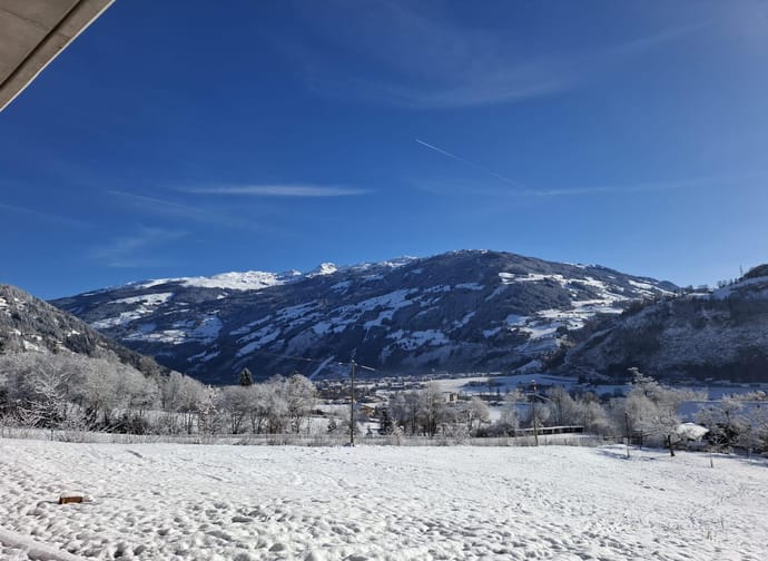 Schneebedeckte Berge unter klarem blauen Himmel, einige Wolken und eine Flugzeugspur sichtbar.