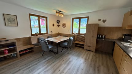 Bright kitchen and dining area with wooden furniture, two windows, and wall decorations.