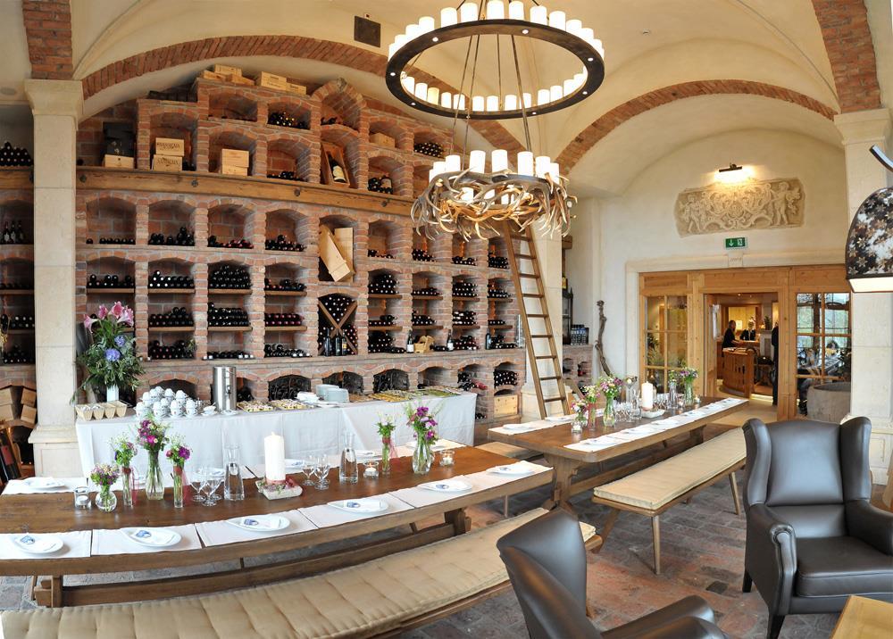 Rustikaler Speiseraum mit langen Tischen, Weinregal aus Ziegeln, Blumen und Kerzen, gemütliche Atmosphäre.