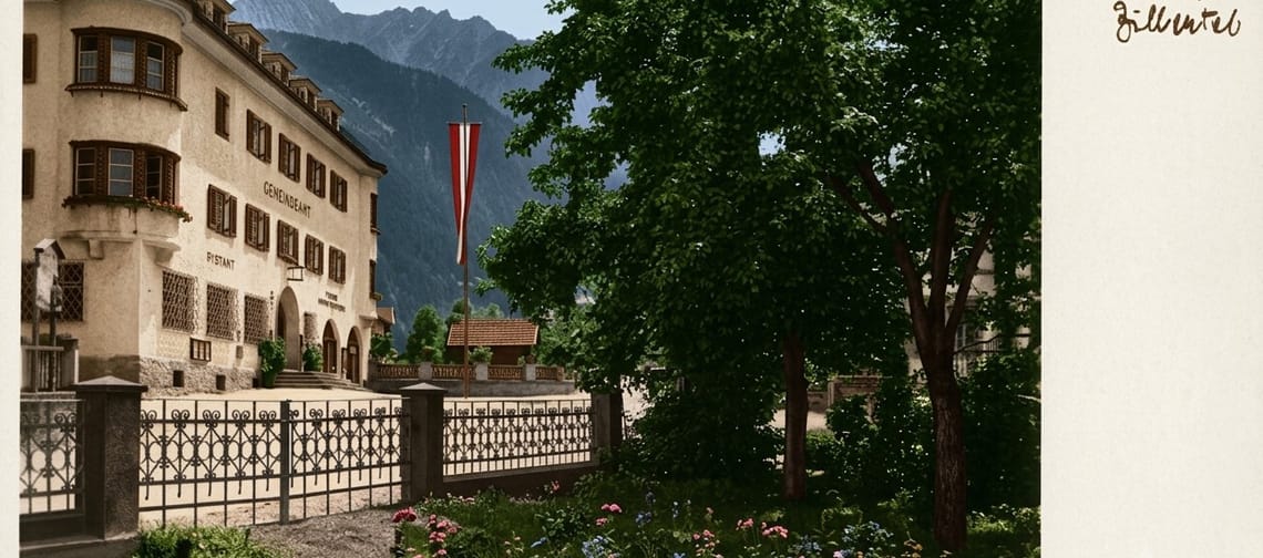 Historic colourised postcard of the municipal office in Mayrhofen, Tyrol: civic building with a fence and large trees in the foreground, with the Zillertal mountains behind.