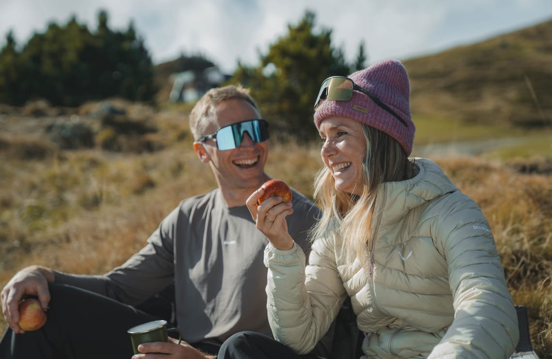 Genussvolle Herbstpause in Mayrhofen ©Mayrhofner Bergbahnen Herbstwanderung in Mayrhofen im Zillertal: Zwei Wanderer sitzen auf einer Almwiese, trinken aus Tassen und genießen die Sonne in der Berglandschaft.