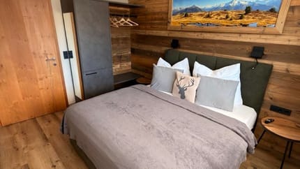 Schlafzimmer mit Holzwand, Bett mit grüner Kopfstütze, Wandbild der Berge, Nachttisch und moderne Deckenleuchte.