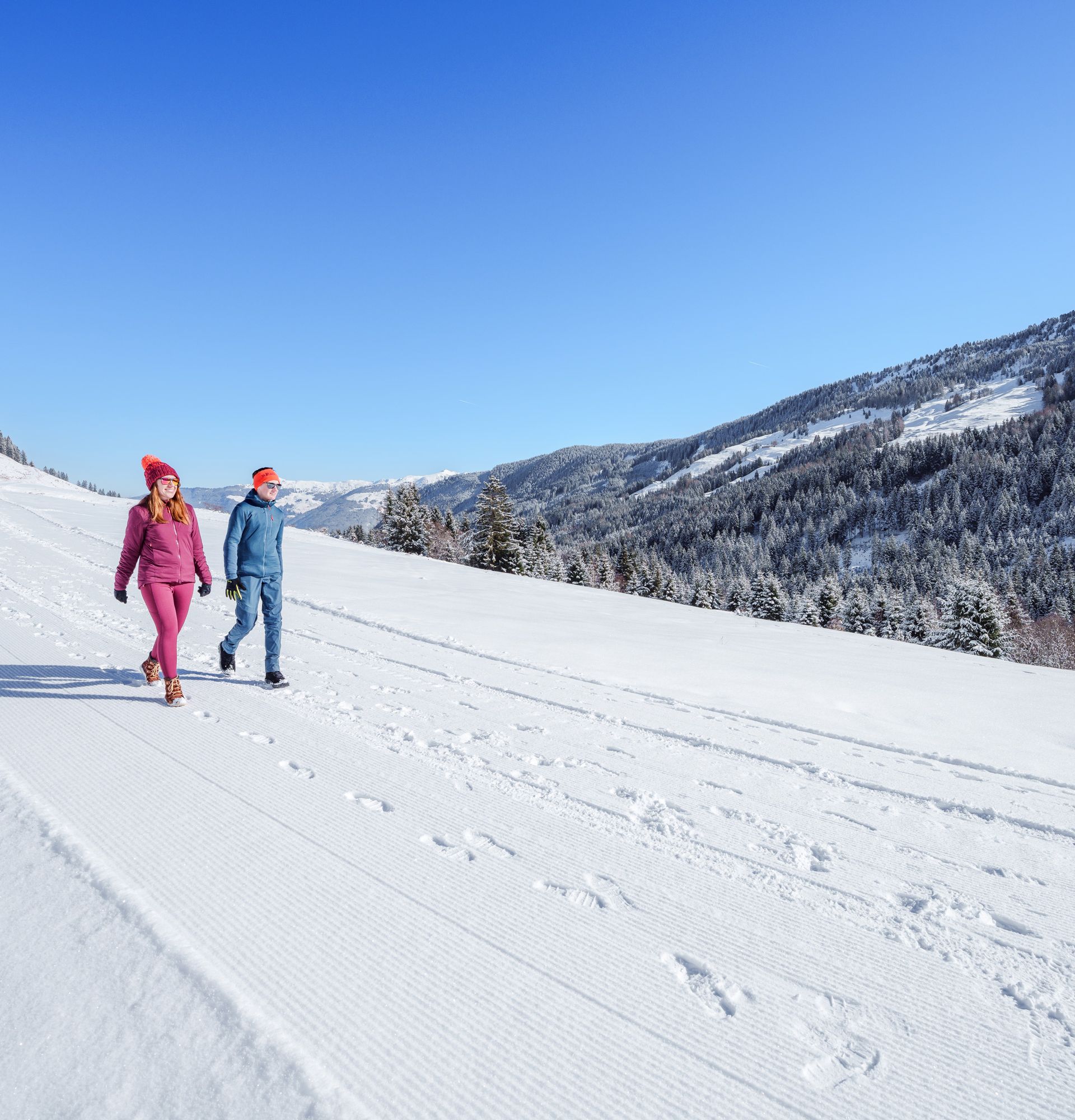 Zwei Menschen wandern in schneebedeckter Berglandschaft bei klarem Himmel.