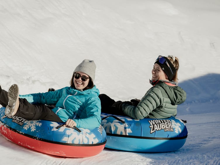 Two people enjoying snow tubing on the dedicated tubing slope at Winterzauber Ginzling in the Zillertal, a fun and family-friendly winter activity in Austria.