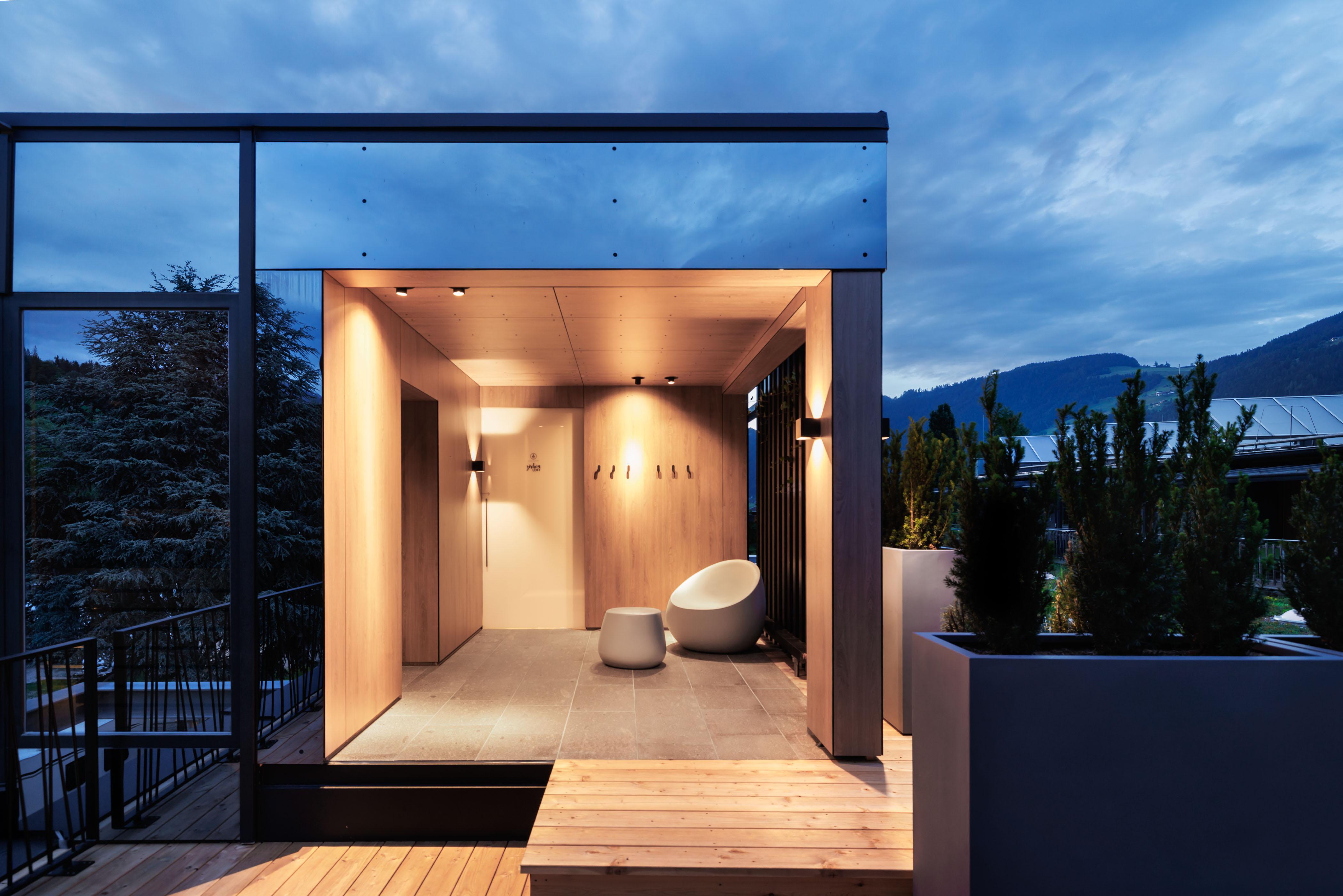 Moderne Terrasse mit Holzverkleidung, bequemen Sitzmöbeln und Blick auf Berge bei Abenddämmerung.