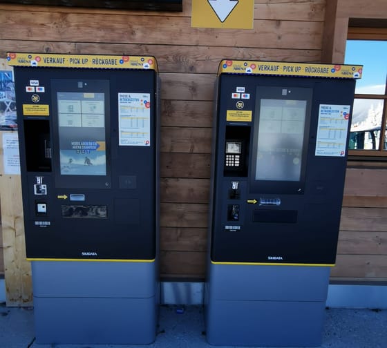 Zwei Skidata Ticketautomaten vor einer Holzwand, mit gelben und schwarzen Akzenten, im Freien.