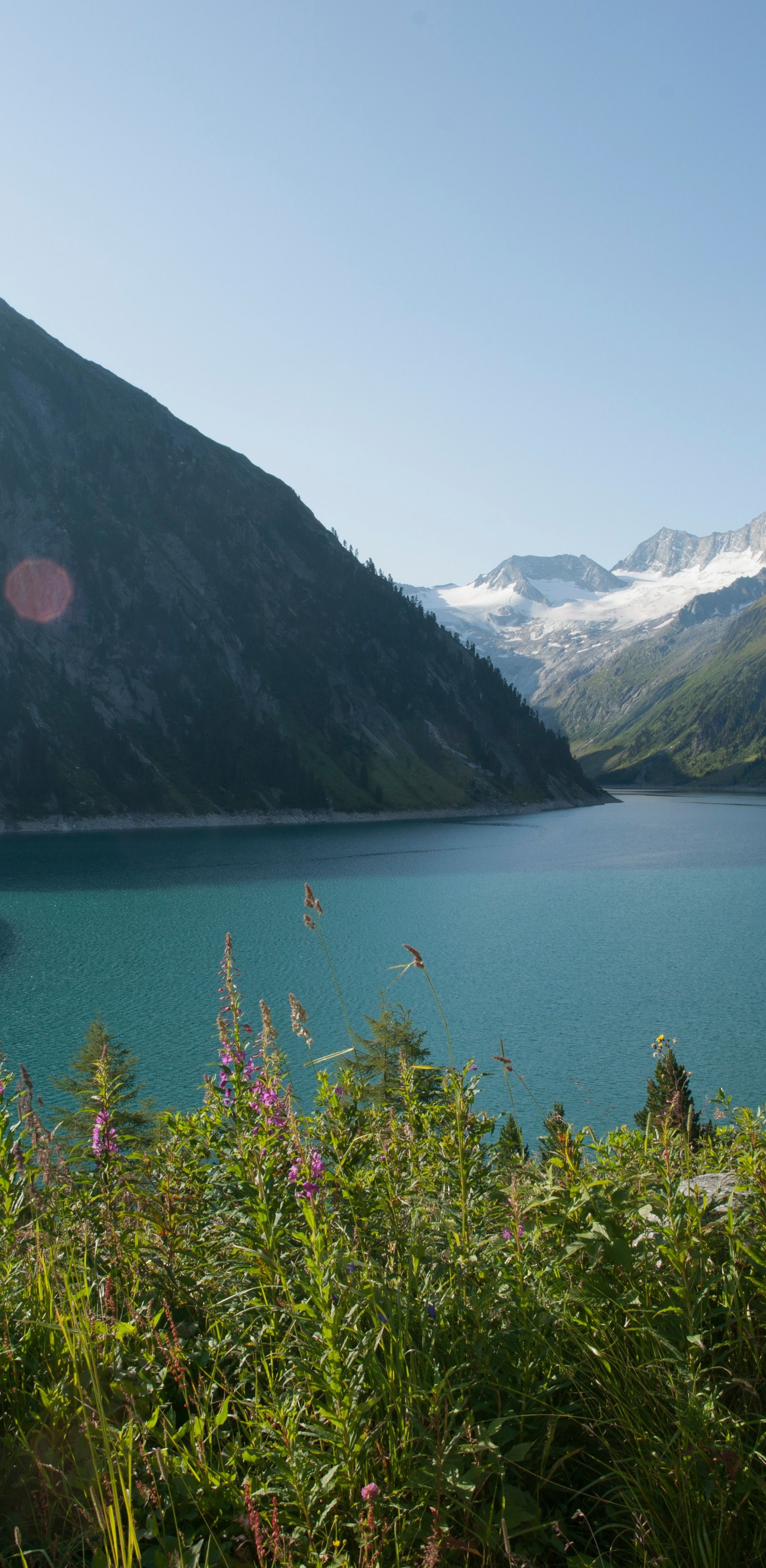 Schlegeisspeicher ©Verbund Eine Frau steht auf einem Aussichtspunkt mit Blick auf den Schlegeisspeicher im Zemmgrund, Zillertal. Vor ihr liegt der türkisfarbene See mit Staumauer, umgeben von Bergen. Sie schaut mit der Hand über der Stirn in die Ferne.