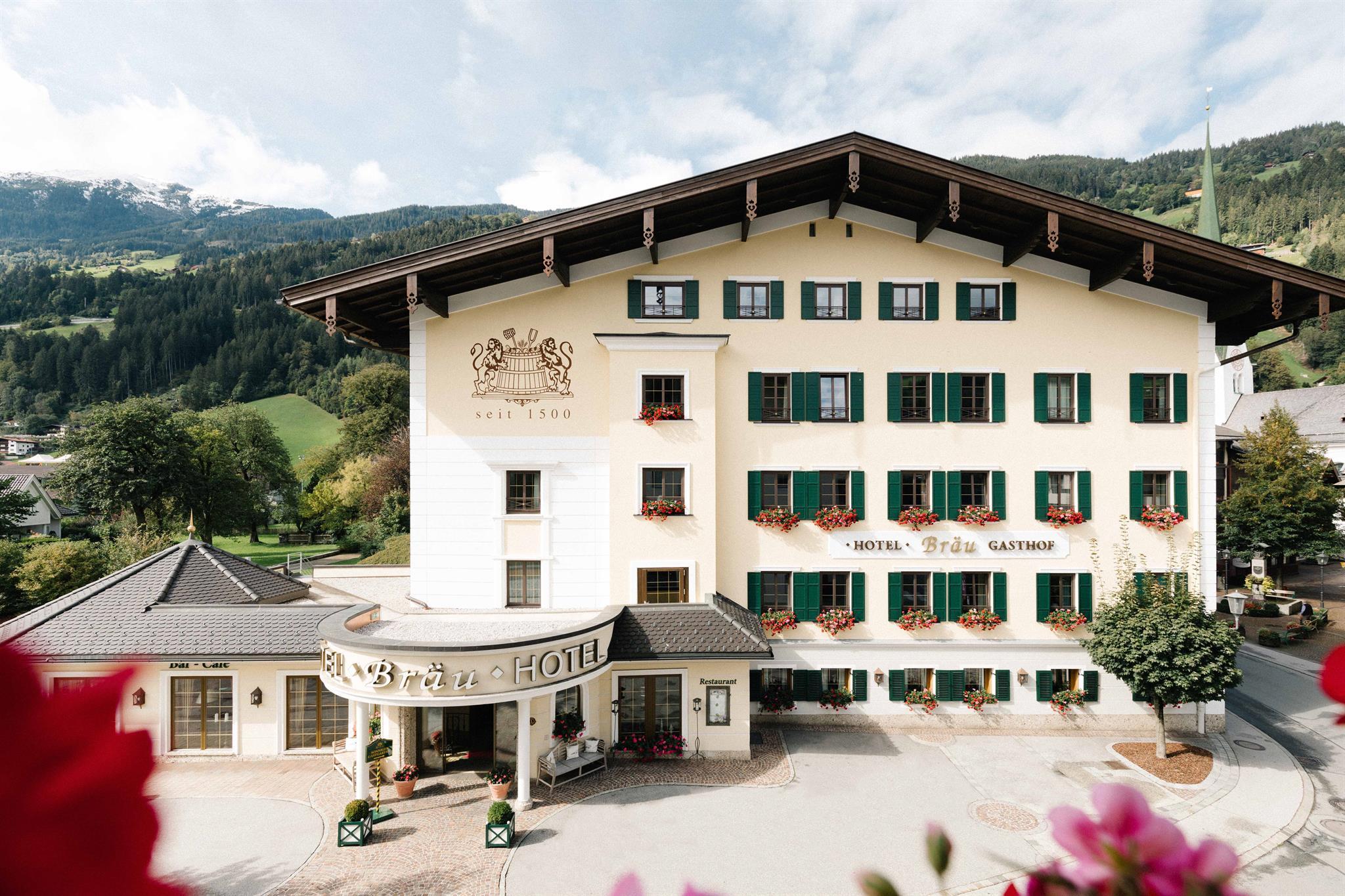 Hotel mit grünen Fensterläden, Blumen und Berglandschaft im Hintergrund, seit 1500 im Betrieb.