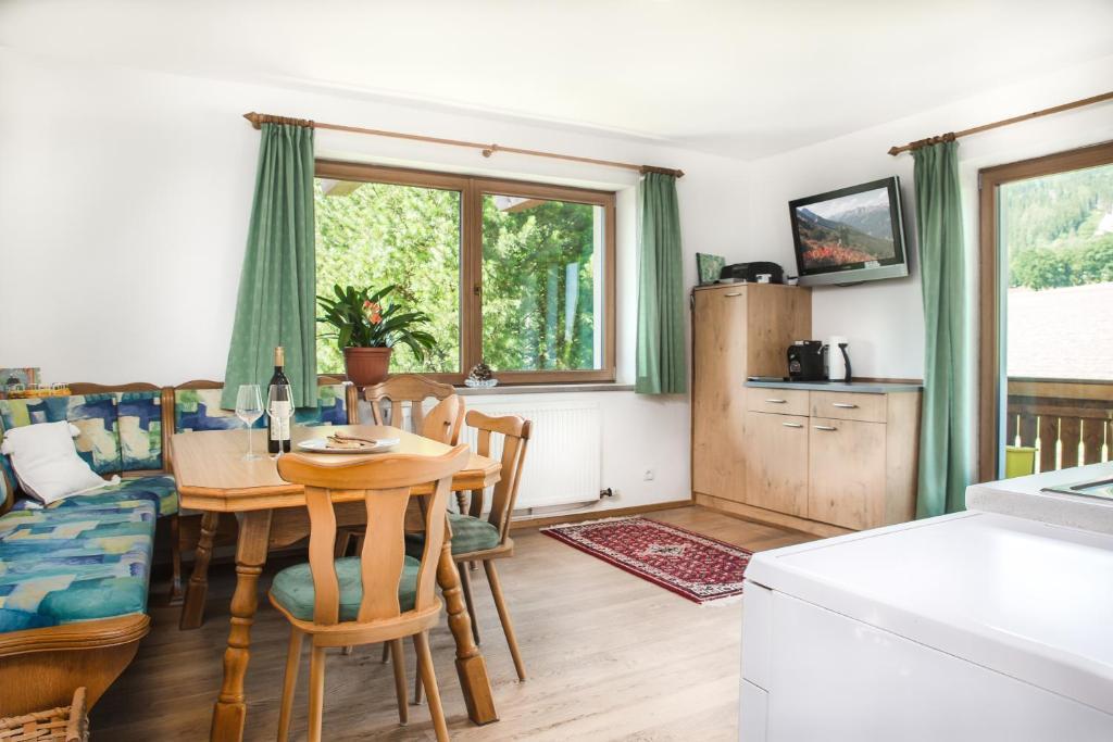 Gemütliches Wohnzimmer mit Esstisch, Stühlen, Fenster mit grünen Vorhängen, Fernseher und Waschmaschine.