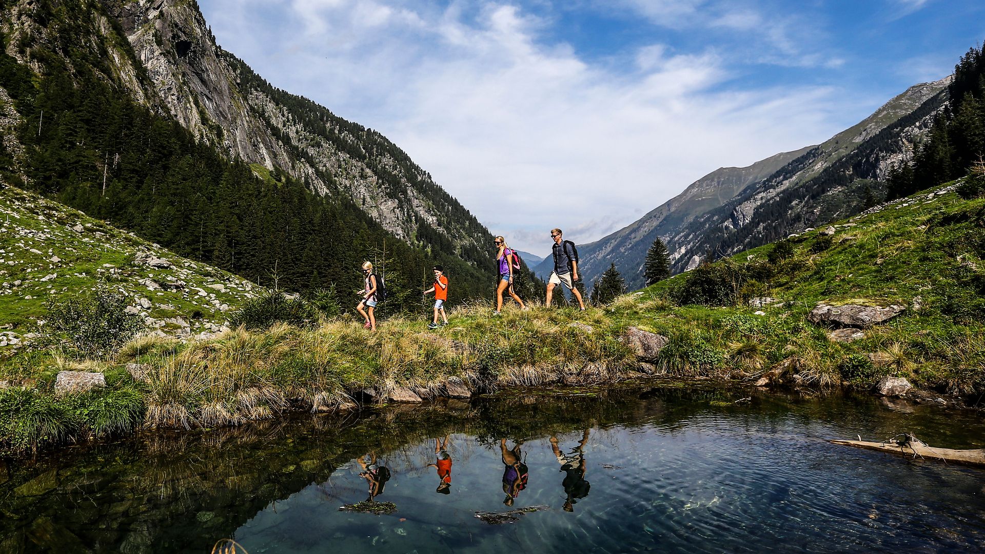 Familie wandert im Stilluptal in der Ferienregion Mayrhofen-Hippach, umgeben von Bergen, Wiesen und einem klaren Bergsee.