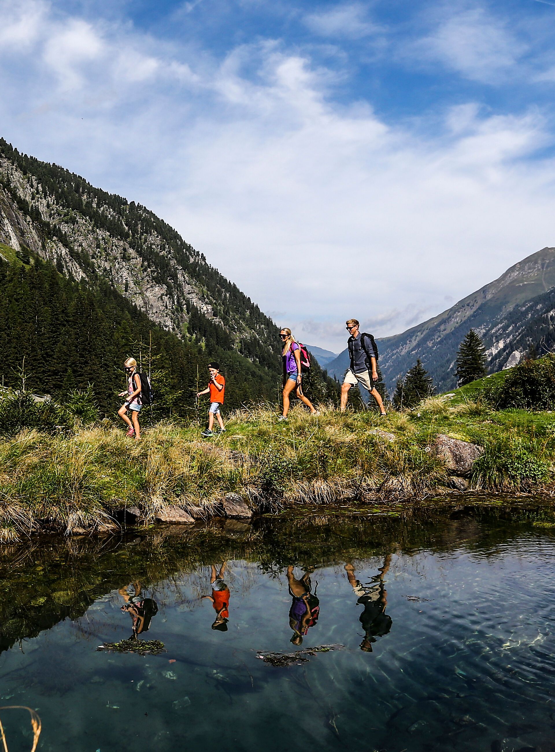 Familie wandert im Stilluptal in der Ferienregion Mayrhofen-Hippach, umgeben von Bergen, Wiesen und einem klaren Bergsee.