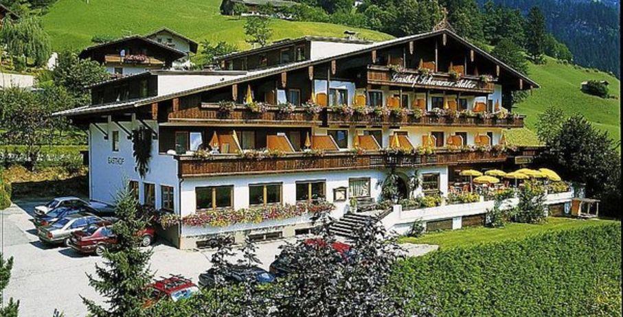 Das Bild zeigt den Gasthof Schwarzer Adler von außen. Vor dem Gebäude erstreckt sich ein offenes Feld, und auf der Terrasse stehen mehrere gelbe Sonnenschirme, die für eine einladende Atmosphäre sorgen.