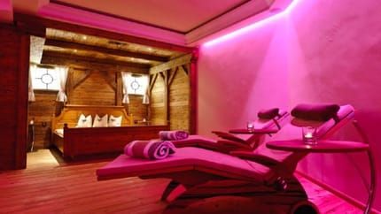The picture shows several massage tables with small tables beside them. Behind them is a wooden bed softly illuminated by pink LED lighting, creating a relaxing atmosphere.