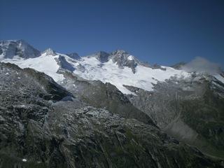 Mountain peaks with snow and glaciers under a clear blue sky, surrounded by rocky terrain.