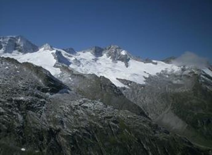 Mountain peaks with snow and glaciers under a clear blue sky, surrounded by rocky terrain.