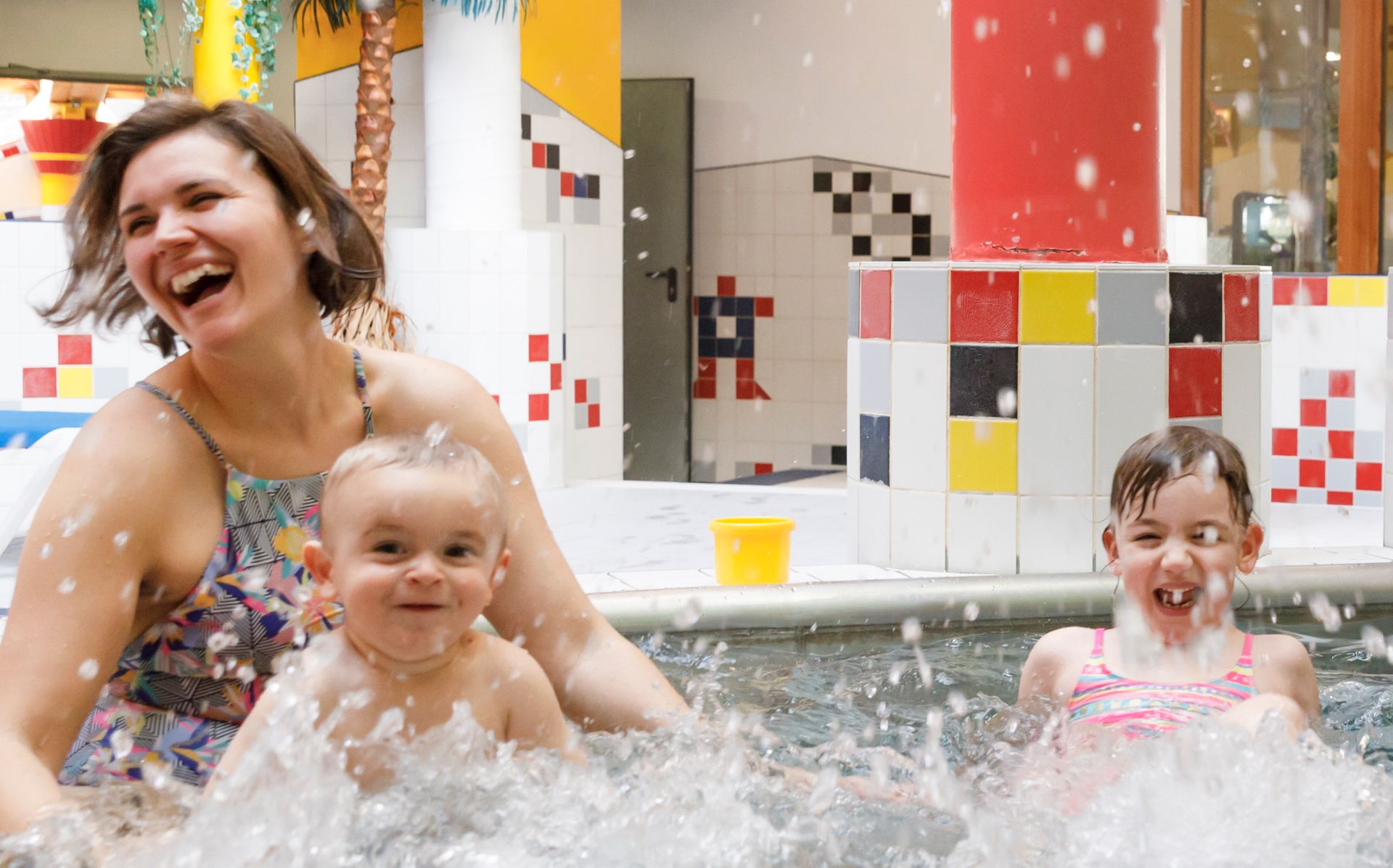 Mutter mit zwei kleinen Kindern beim Baden und Lachen im Erlebnis-Hallenbad Mayrhofen – familienfreundlicher Badespaß im Zillertal.