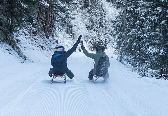 Zwei Personen fahren mit der Rodel auf einer präparierten Rodelbahn