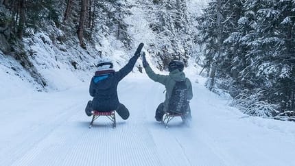 Zwei Personen fahren mit der Rodel auf einer präparierten Rodelbahn
