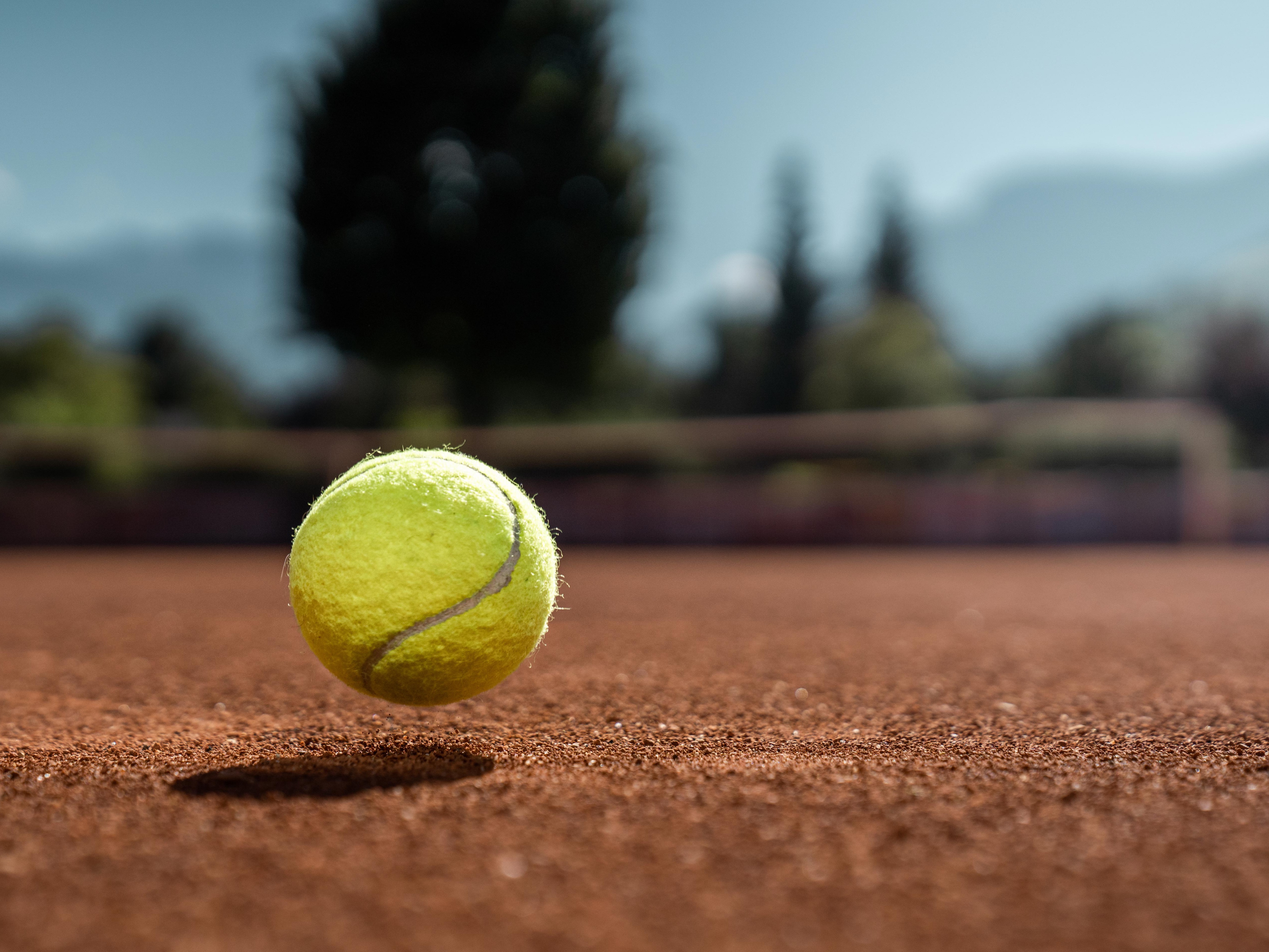 Tennisball auf Sandplatz vor Bergkulisse – Symbolbild für Tennissport in der Sommerwelt Hippach im Zillertal, Tirol.