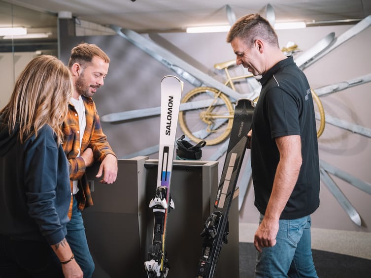 Skiverleih im Zillertal, Tirol: Mitarbeiter stellt am Servicegerät die Skibindung ein, während Gäste ihre Ausrüstung für den Winterurlaub in Mayrhofen-Hippach auswählen.