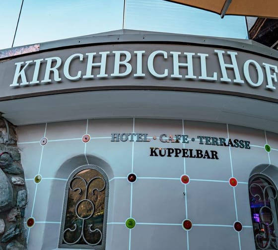 Schild mit kyrillischer Schrift über einem Eingang, umgeben von Steinen und bunten Dekorationen, im Freien.