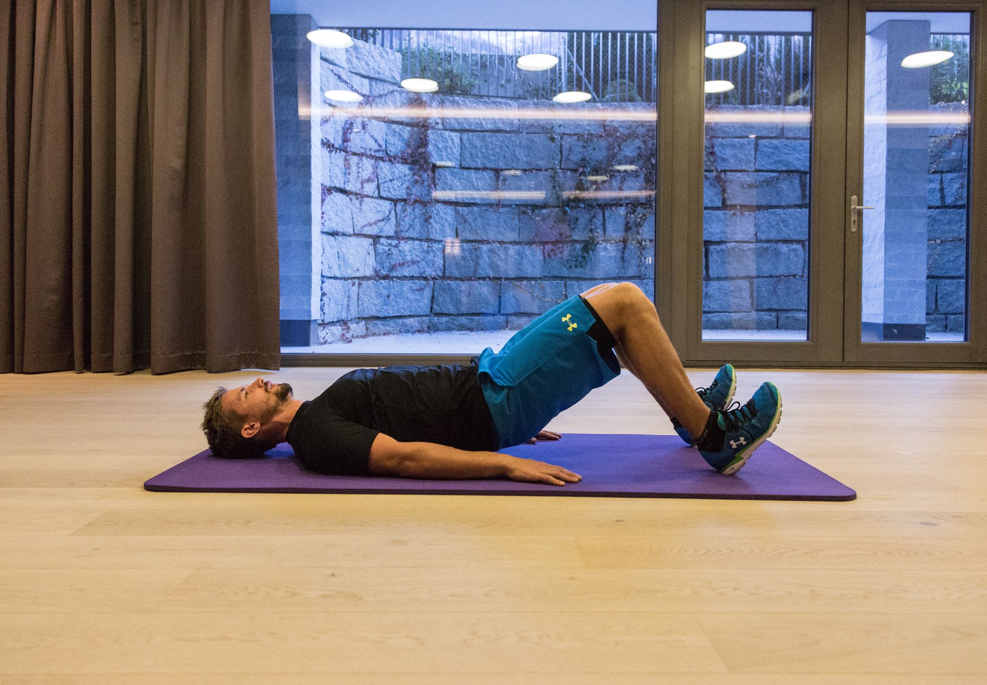 Man performing glute bridge exercise on yoga mat in training hall in Mayrhofen. Ski fitness training with Christoph Ebenbichler – strengthens back, legs and core for a fit start to the winter season.