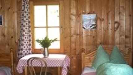 Cozy wooden room with window, table with red checkered cloth, chair, plant, and couch with green pillows.