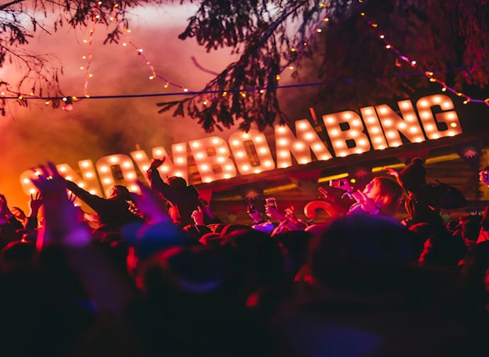 The image shows a celebrating crowd at the forest festival grounds against a black and pink background.
