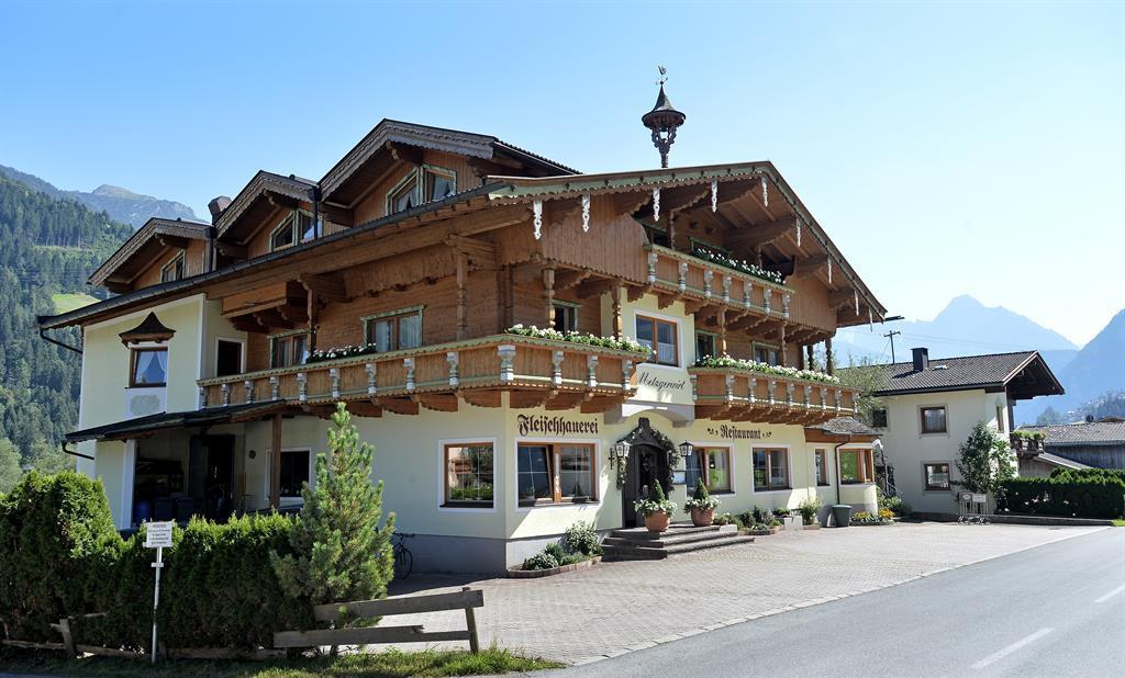 The picture shows Metzgerwirt from the outside. In the background, impressive mountains rise into the blue sky, creating a classic Alpine setting.