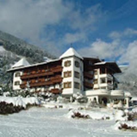 Das Bild zeigt das Hotel Ferienschlössl Alpenblick von außen im Winter. Das Gebäude ist von einer weißen Schneedecke umgeben, und die winterliche Landschaft mit kahlen Bäumen und Bergen im Hintergrund schafft eine ruhige, kalte Atmosphäre.