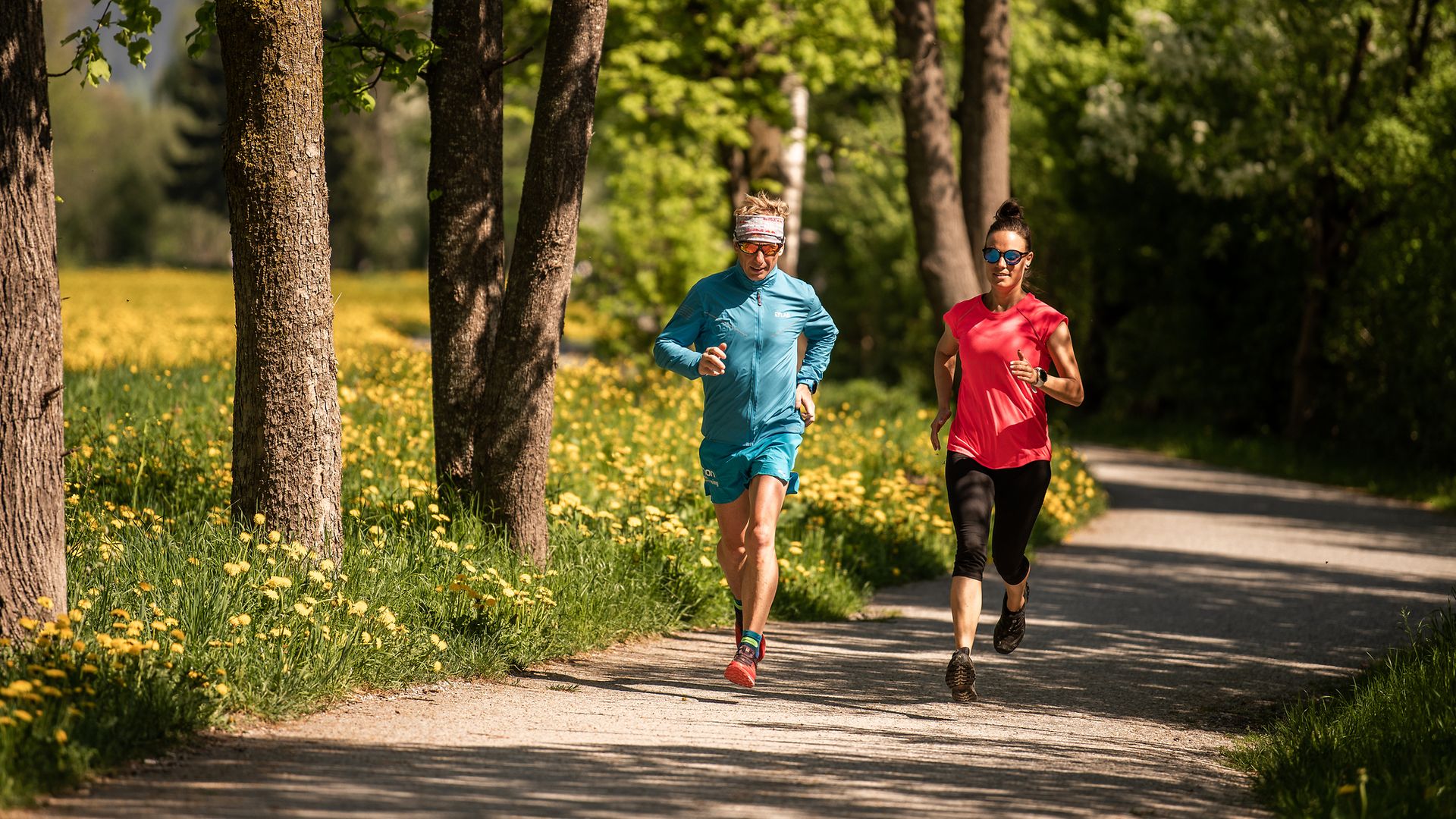 Two people jogging on the Easy Trail in the Mayrhofen-Hippach holiday region, Zillertal. The path winds through green scenery with trees and flowers. Outdoor fitness in nature.