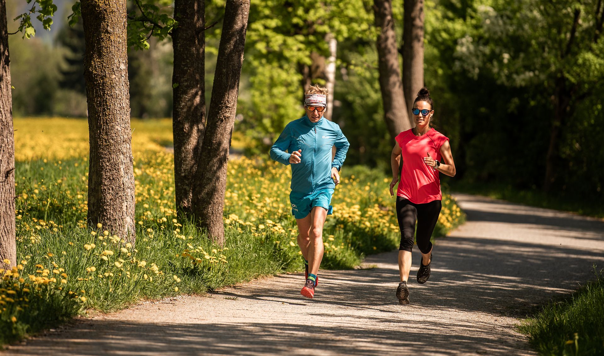 Two people jogging on the Easy Trail in the Mayrhofen-Hippach holiday region, Zillertal. The path winds through green scenery with trees and flowers. Outdoor fitness in nature.