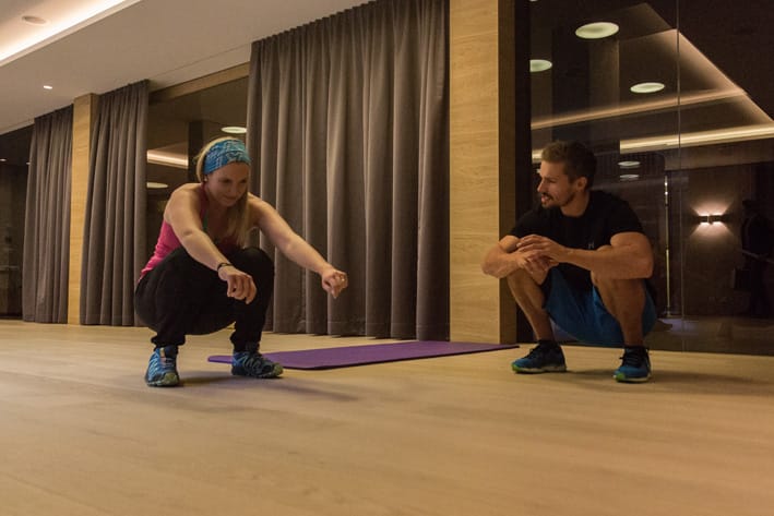 Man and woman in deep squat position in training room in Mayrhofen. Christoph Ebenbichler demonstrates mobility and strength exercise for hips and legs to improve ski fitness.