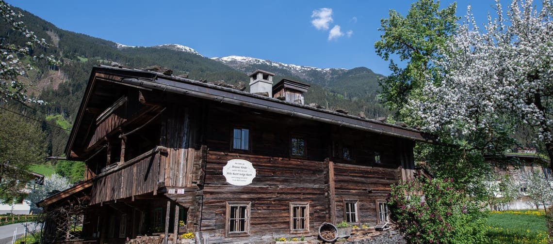Das Bild zeigt das Museum Strasserhäusl in Laimach mit blühenden Bäumen im Hintergrund.