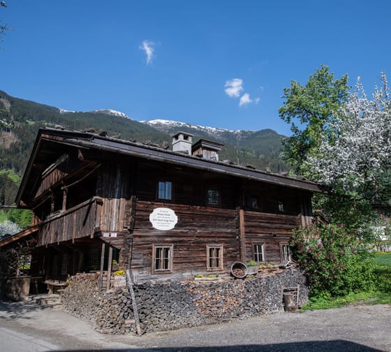 The image shows the Strasserhäusl Museum in Laimach with blooming trees in the background.
