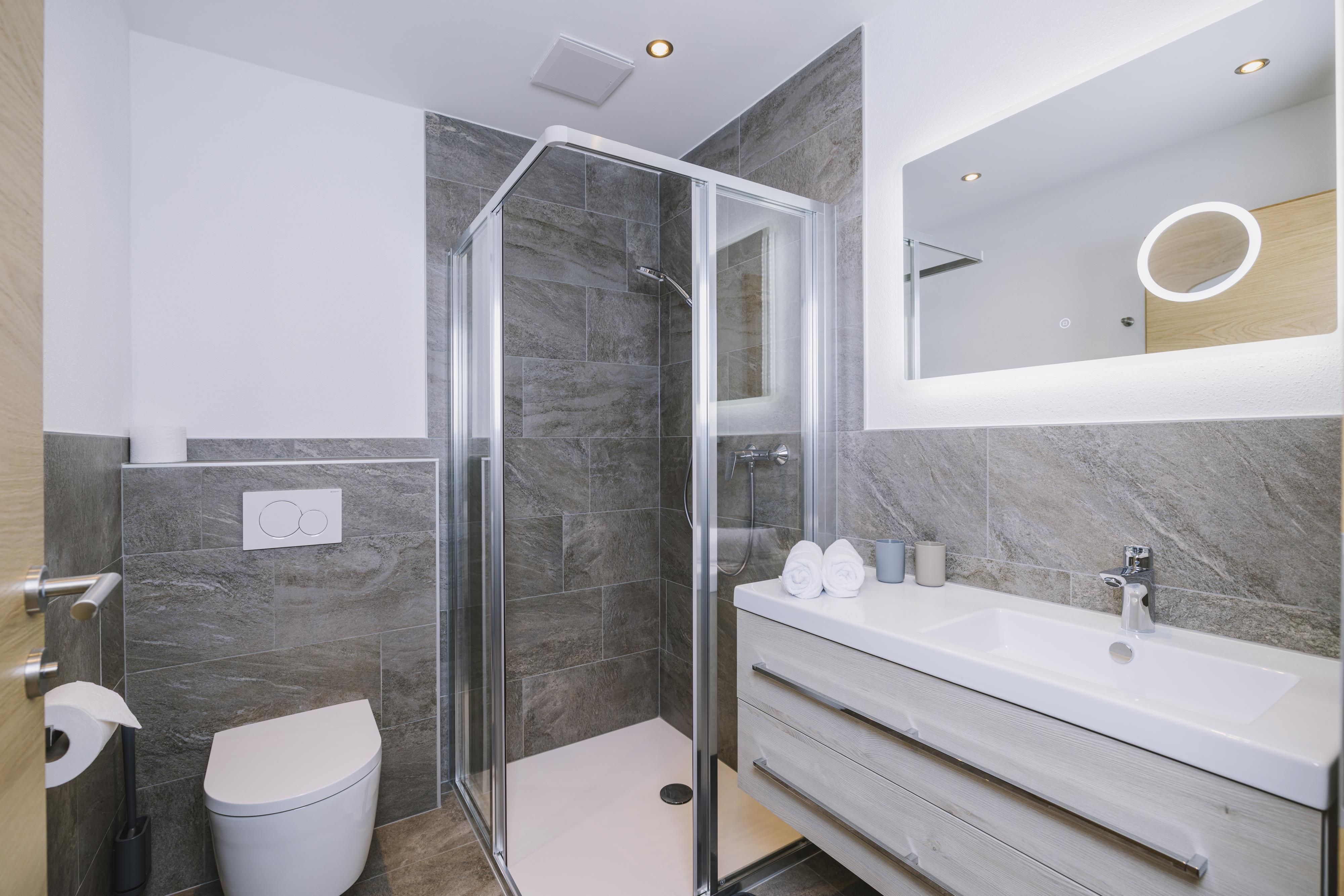 Modern bathroom with shower, sink, mirror, towels, and toilet in neutral tones.